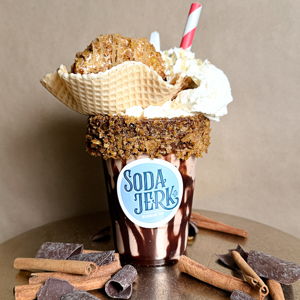 Lucha Libre Lucha Libre shake in a Soda Jerk cup, surrounded by cinnamon sticks and chocolate.