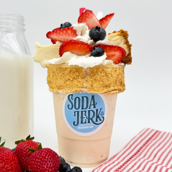 Liberty Cheesecake Shake Liberty Cheesecake Killer Shake in a Soda Jerk cup surrounded by fresh fruit and a bottle of milk.