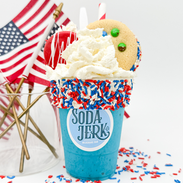 Yankee Doodle Yankee Doodle Killer Shake in a Soda Jerk cup surrounded by sprinkles and American flags in a vase.